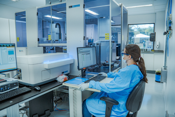 A woman sits at a research desk in full PPE looking at results.