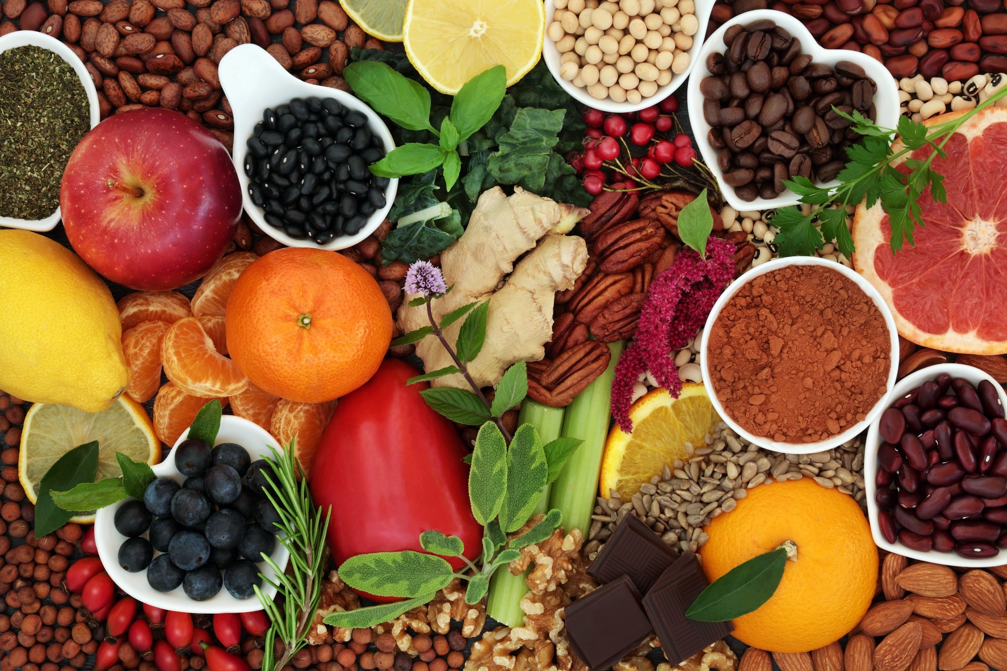 assortment of healthy foods arranged closely together, including fresh fruits, vegetable, nuts, seeds and dried beans