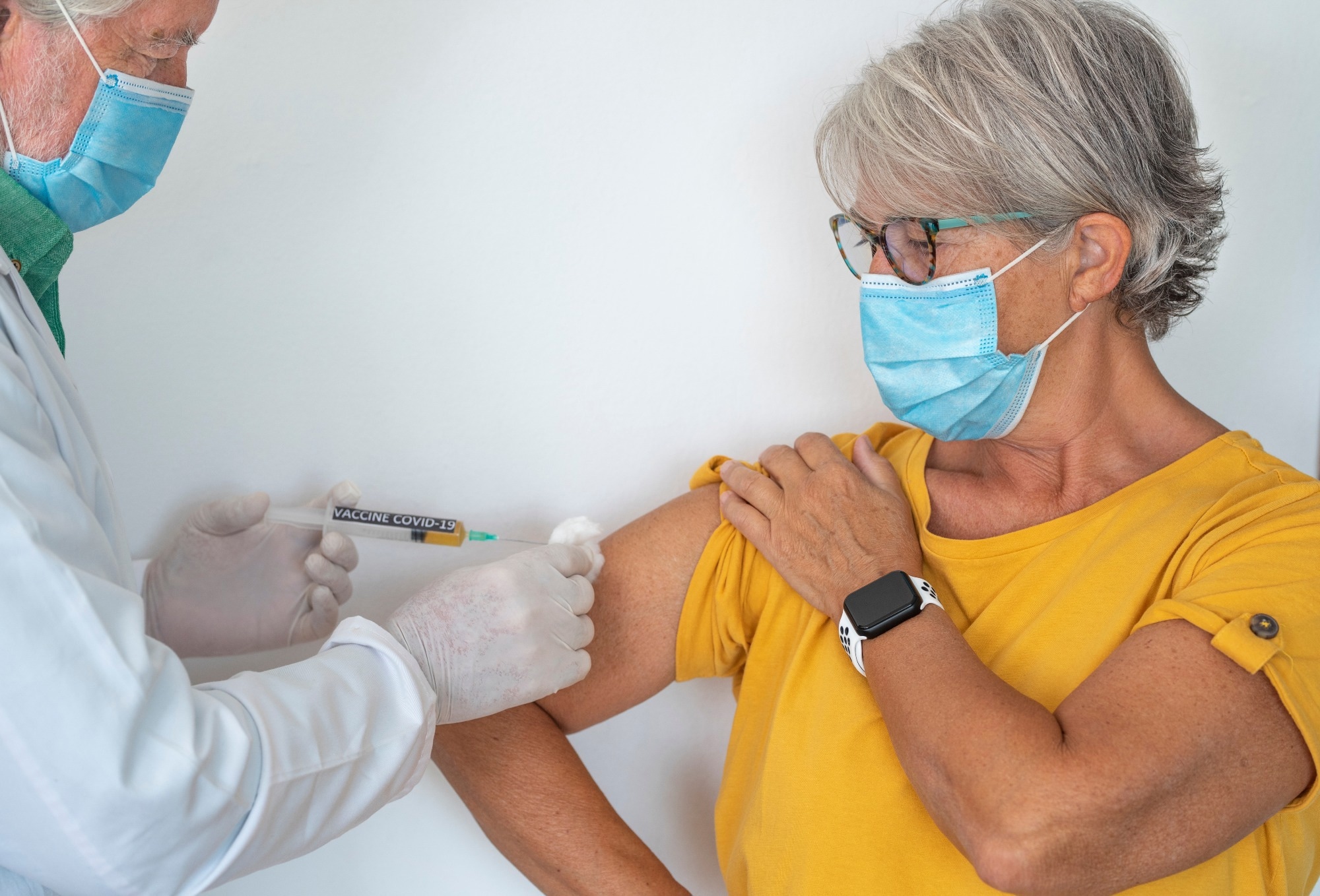 Booster Coronavirus. A syringe in the hands of a doctor injecting the covid-19 coronavirus vaccine to a woman in a yellow shirt