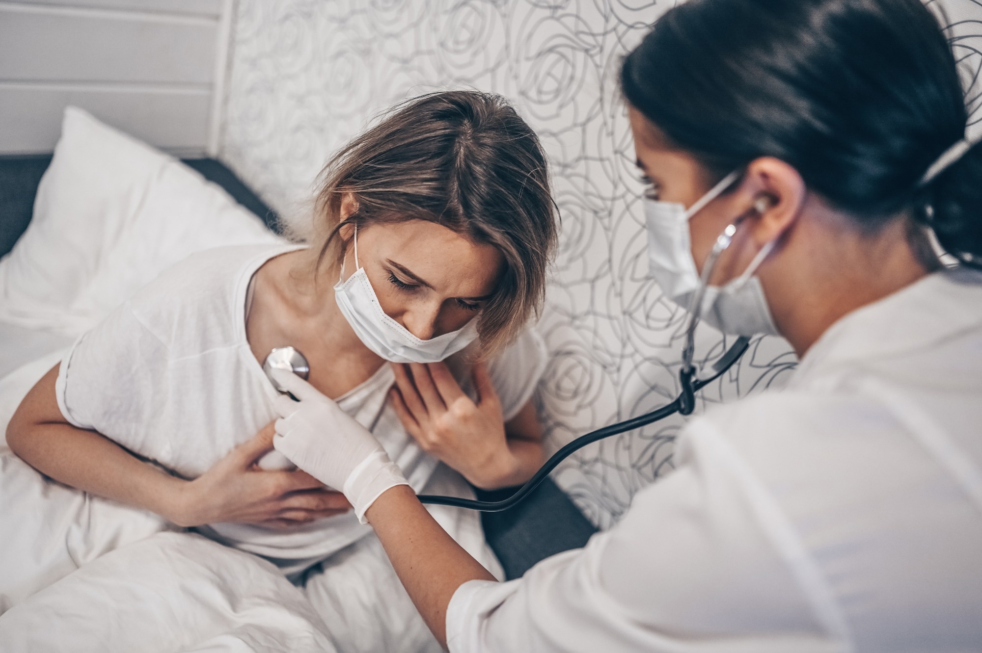 Doctor nurse in protective face mask listening to breath with a stethoscope suspecting Coronavirus (COVID-19)