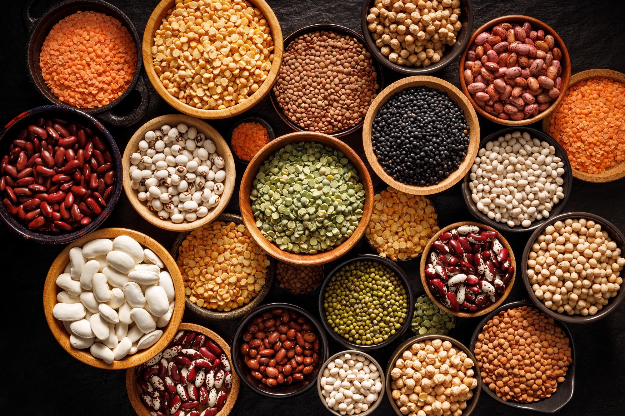 Legumes, a set consisting of different types of beans, lentils and peas on a black background, top view