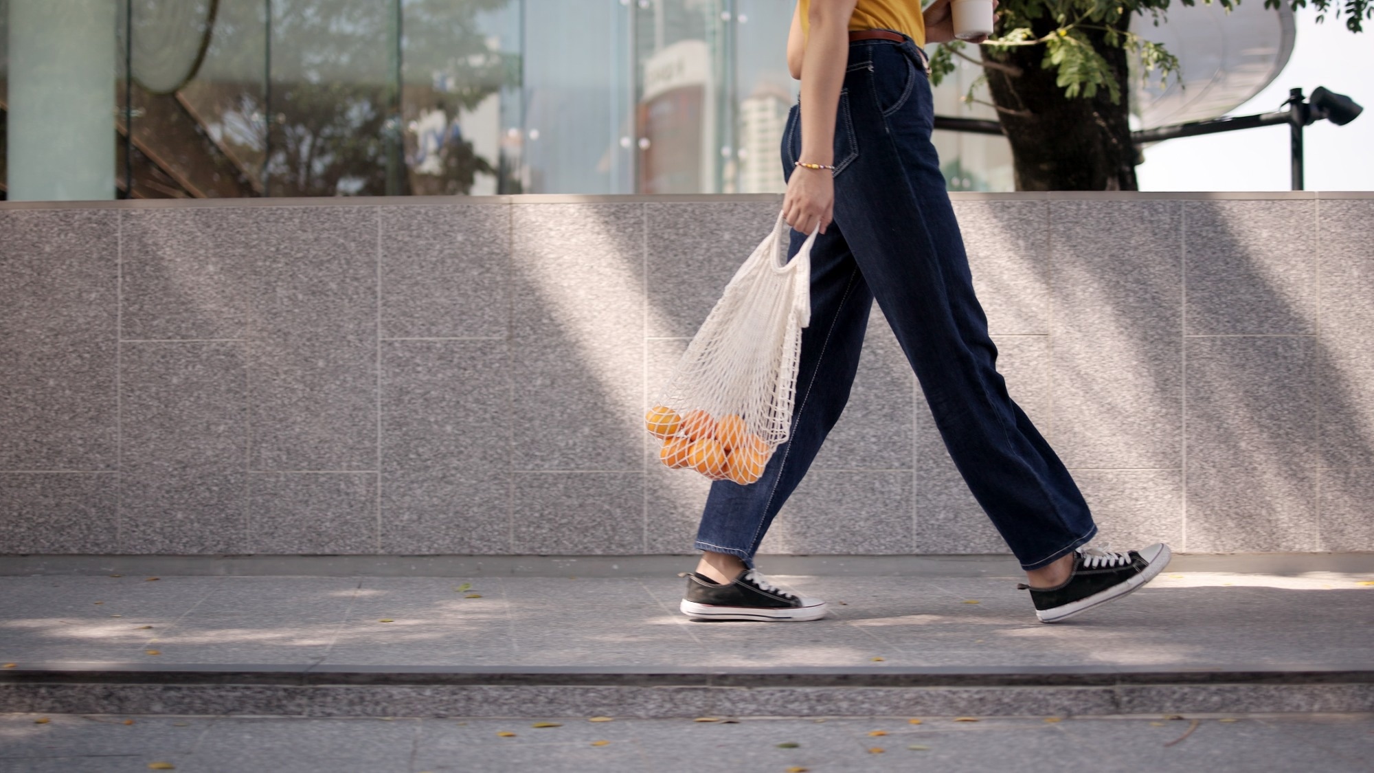 young woman walking carrying a shopping bag of oranges