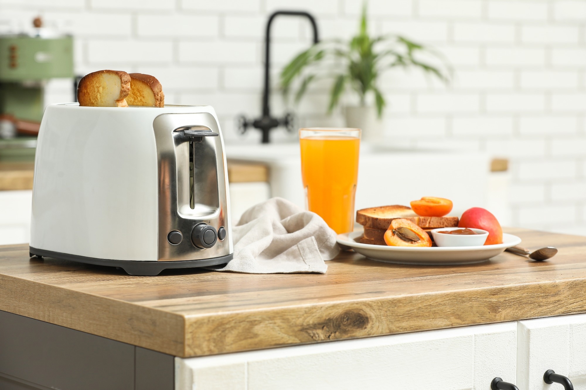 White toaster and plate with bread slices on wooden table in kitchen