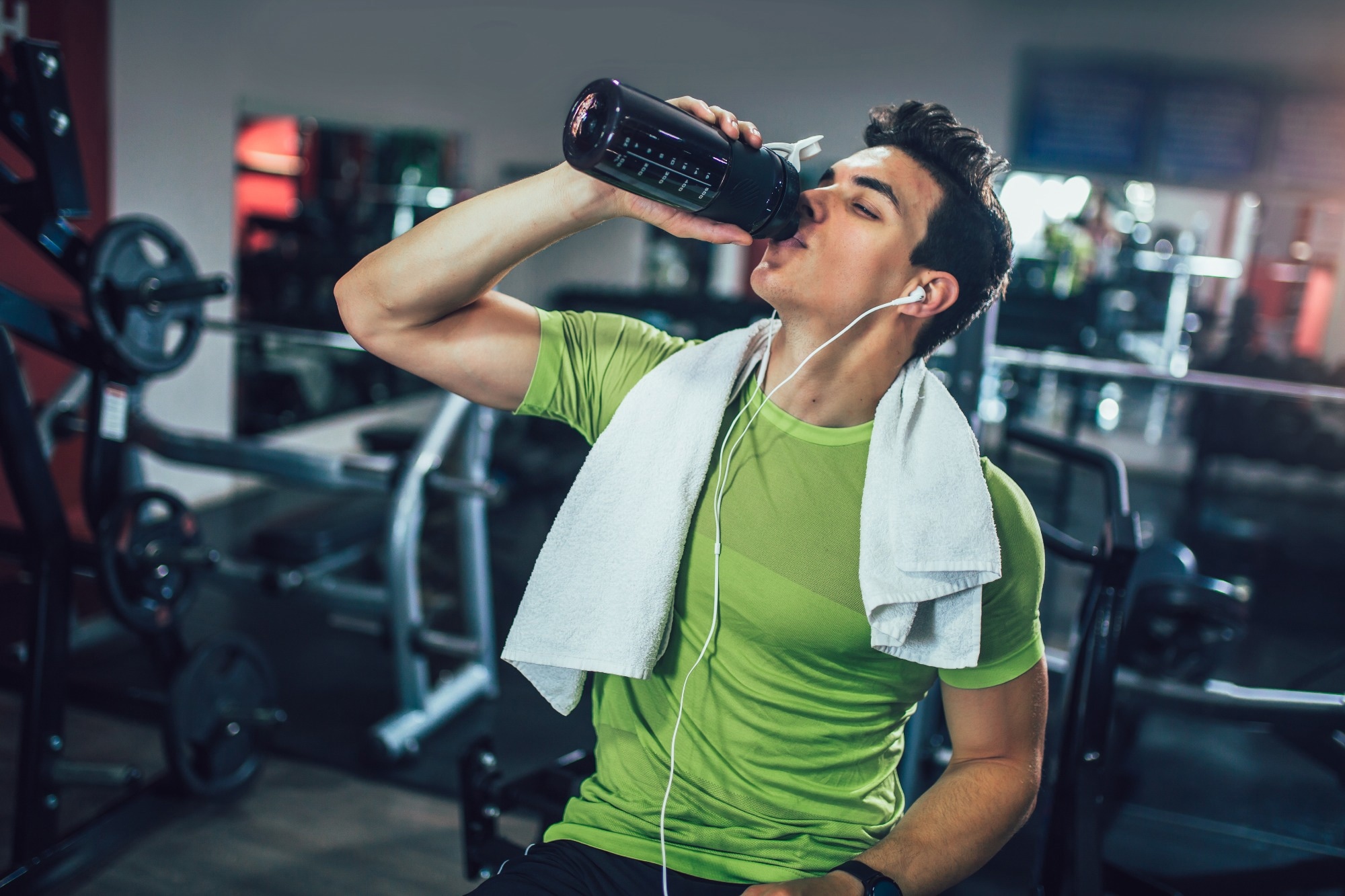Young man drinking pre-workout drink from bottle in the gym