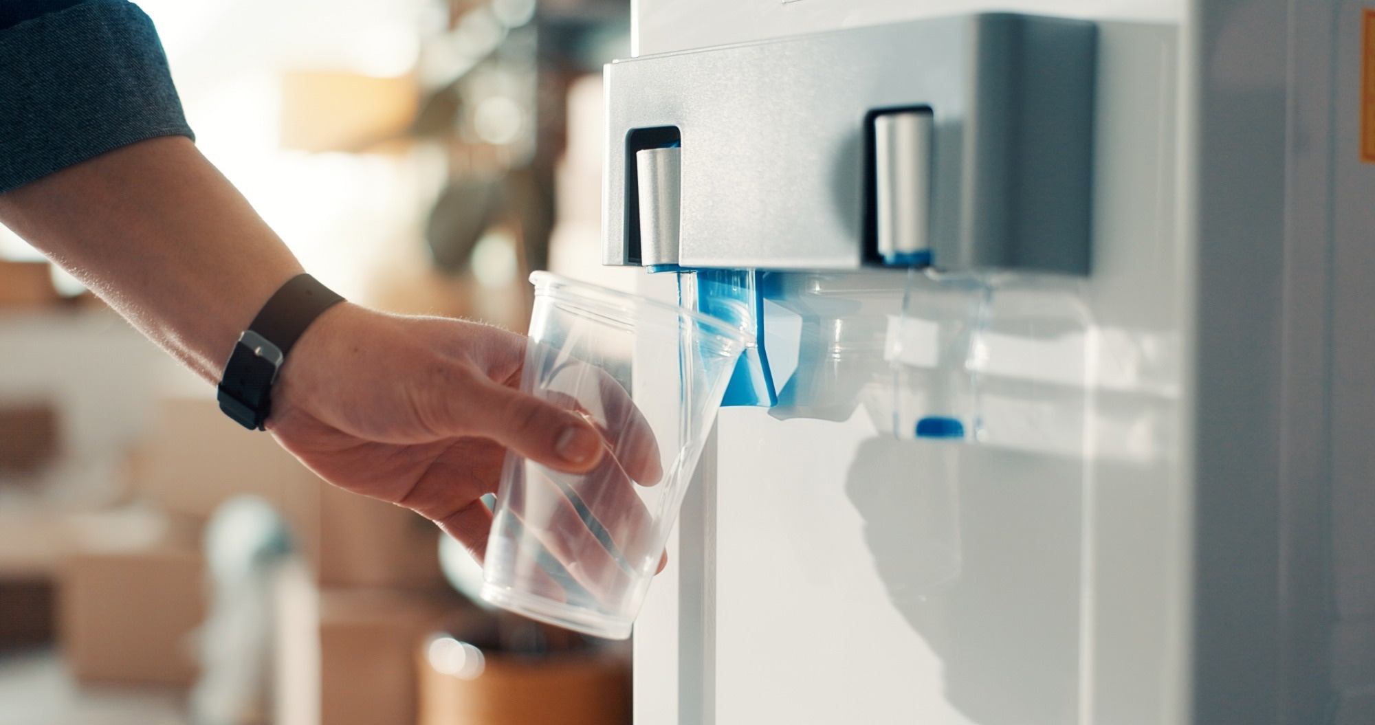 Persons hand holding plastic cup against a water dispenser machinee